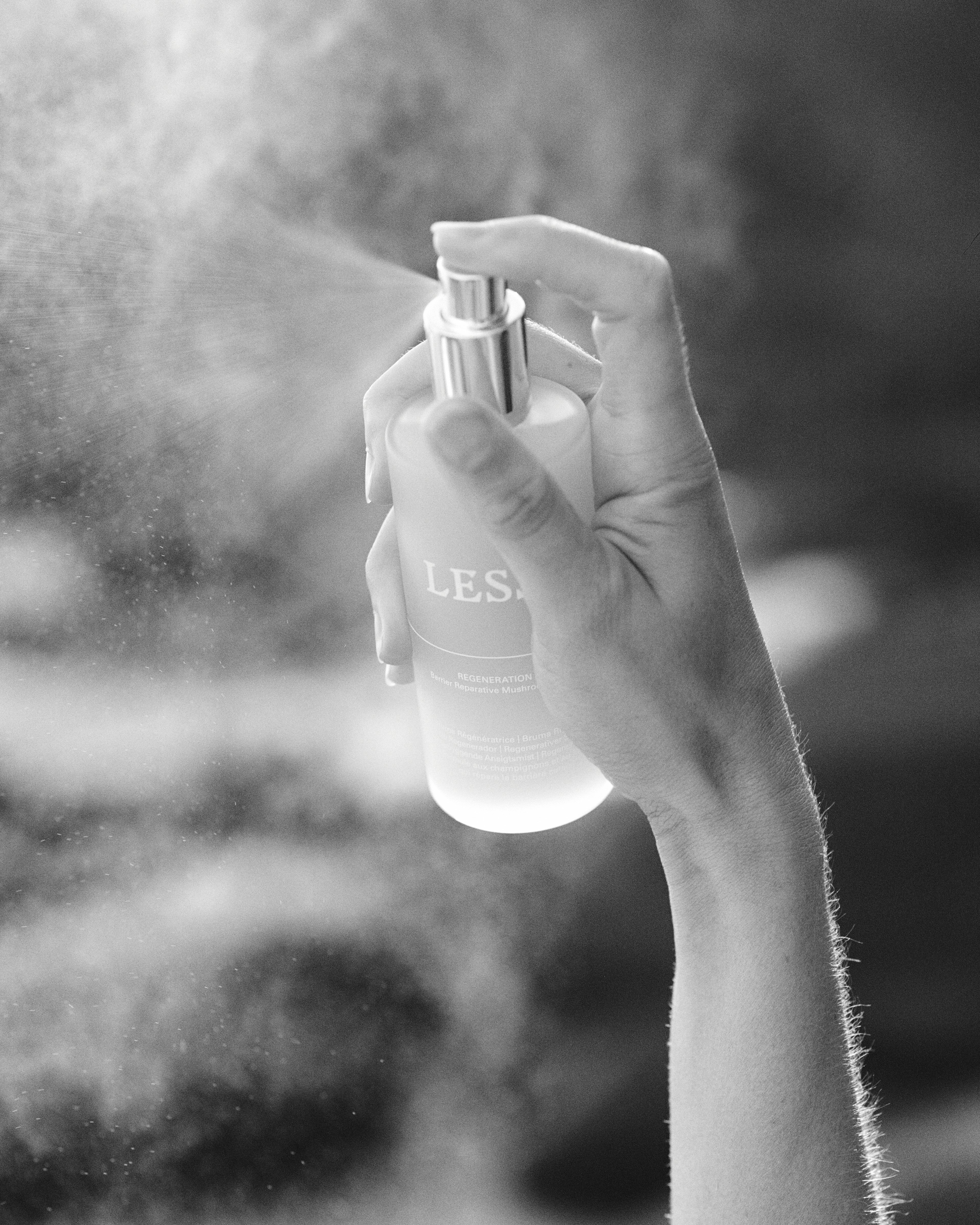 Hand holding a spray bottle labeled 'LESSE' with a blurred background