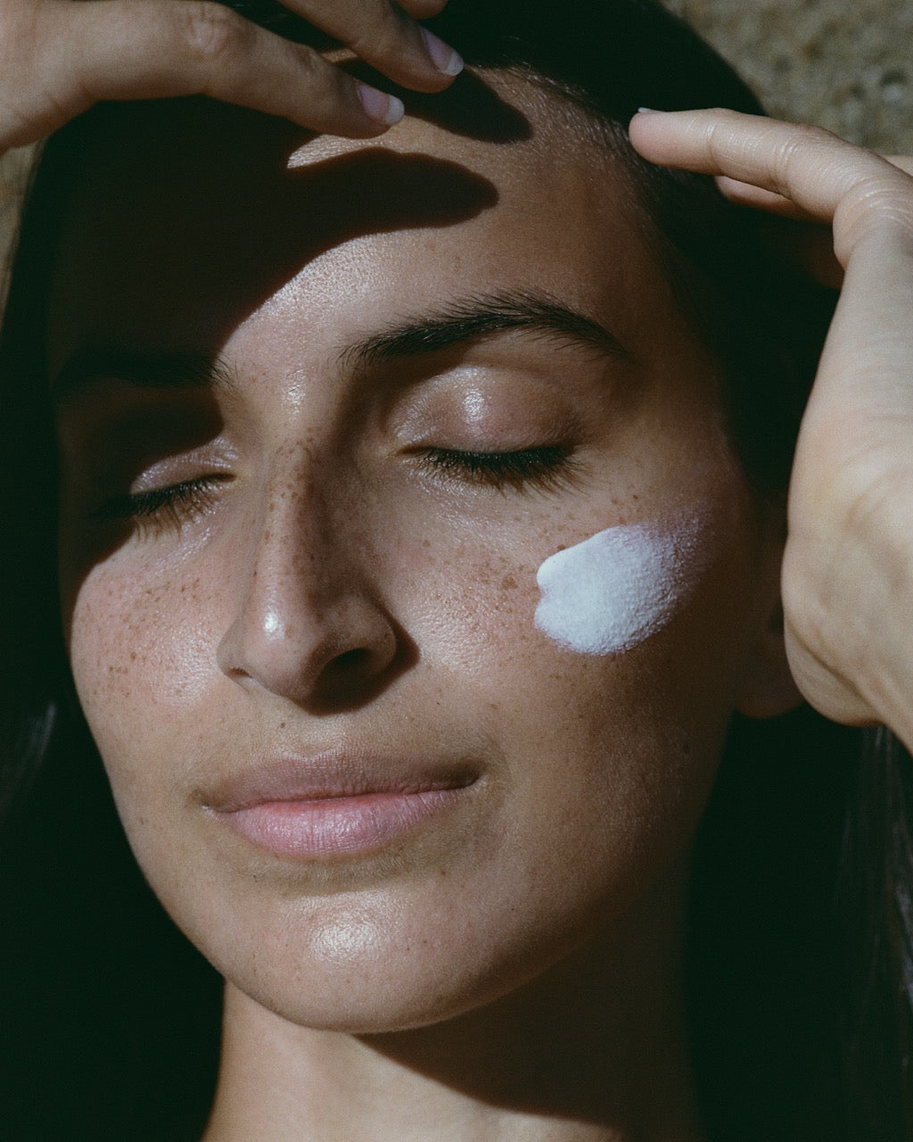 Woman applying sunscreen to her face with a close-up focus on her skin.