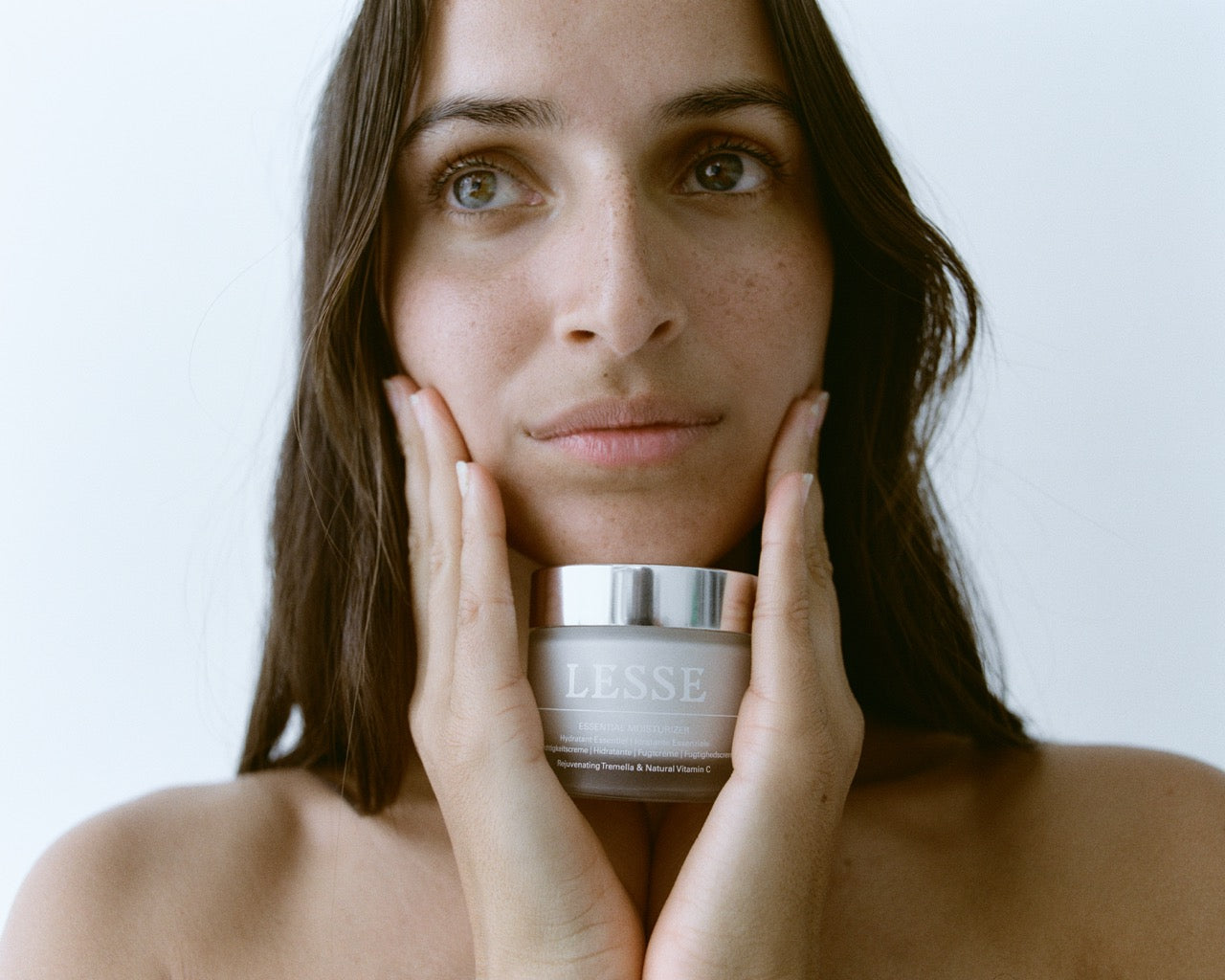 Woman holding a jar of Lesse skincare product against a neutral background