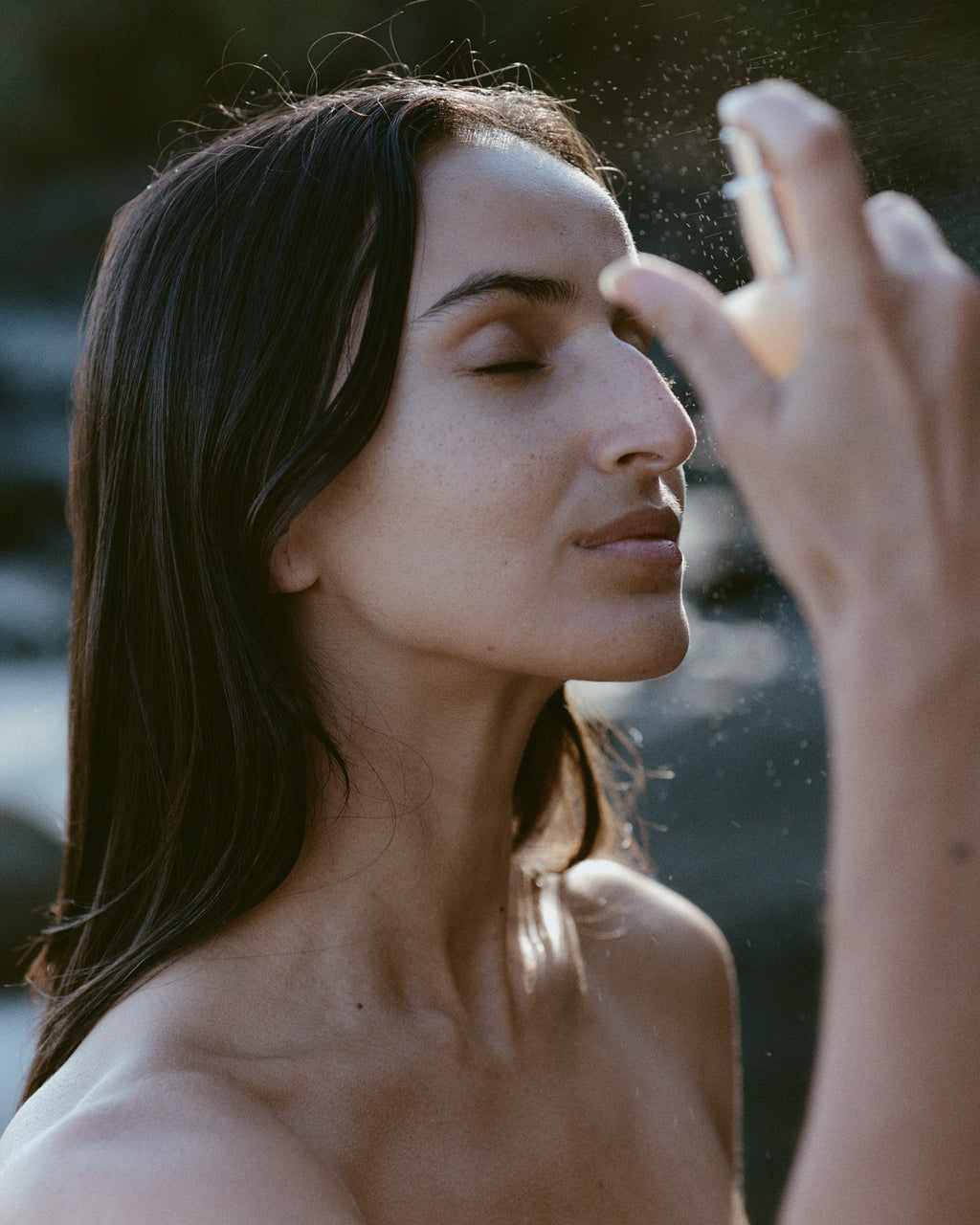Woman applying Regeneration Mist to her face with a blurred natural background