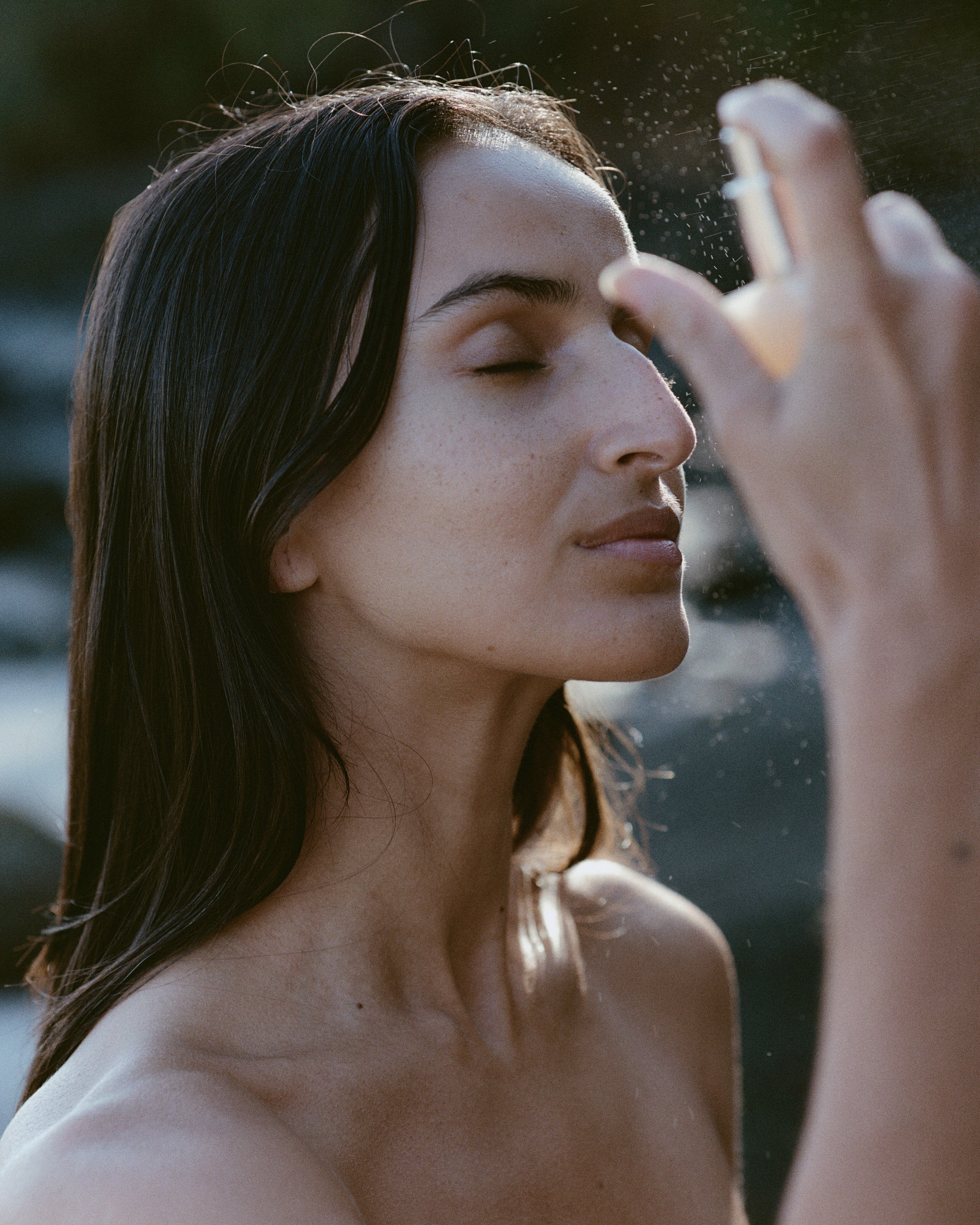 Woman applying Regeneration Mist to her face with a blurred natural background