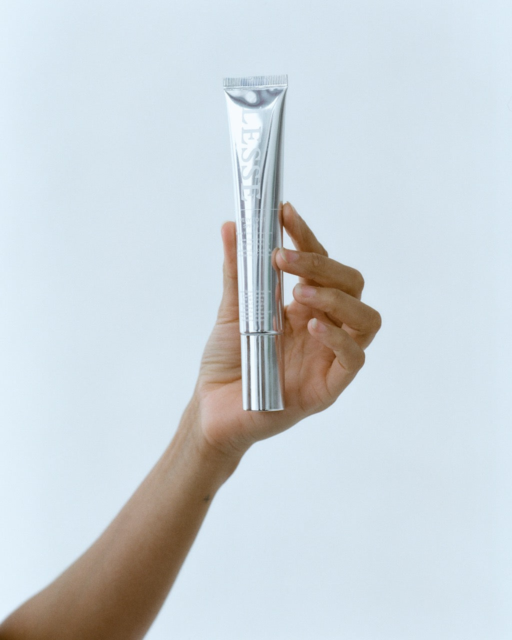 Hand holding a silver LESSE SPF tube against a light blue background