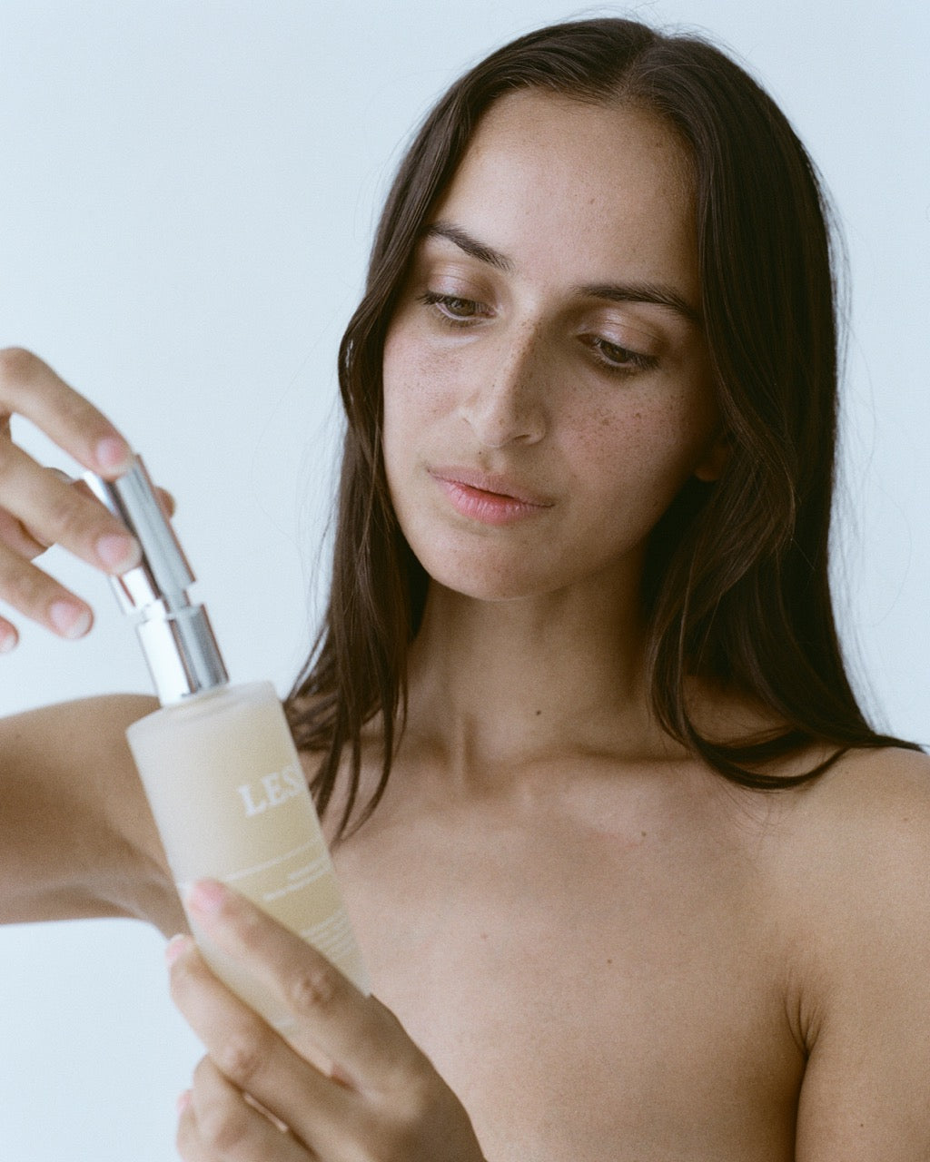 Woman holding a skincare bottle with a plain background