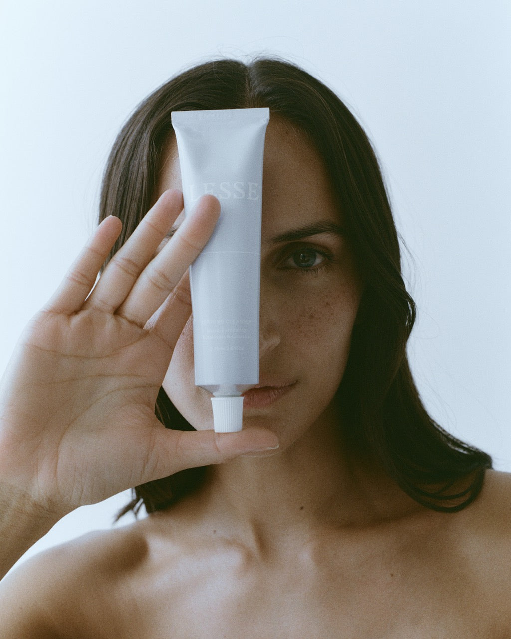 Woman holding a white skincare tube with 'LESSE' branding against a light background