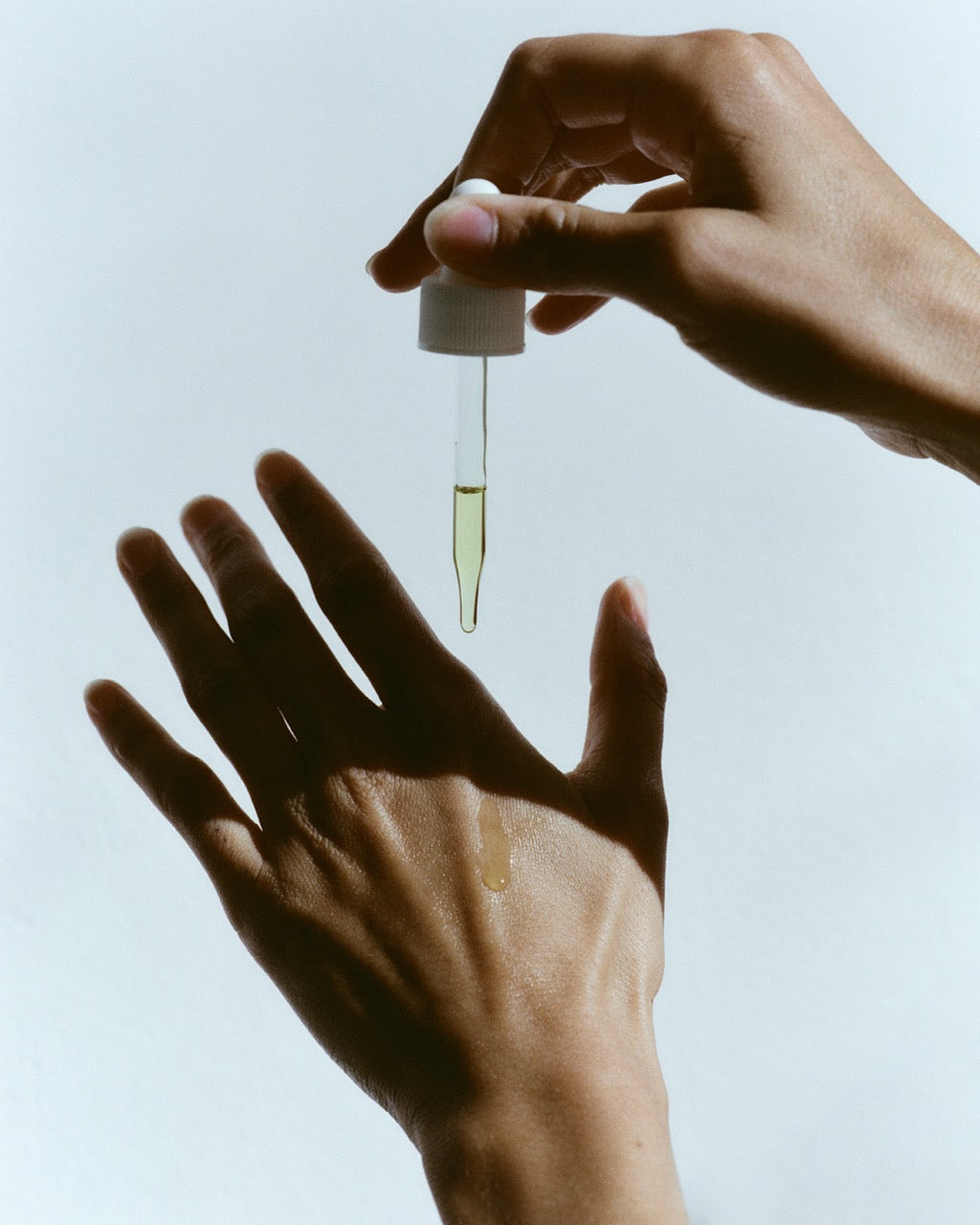 Hand holding a dropper with a small amount of liquid over another hand against a light background