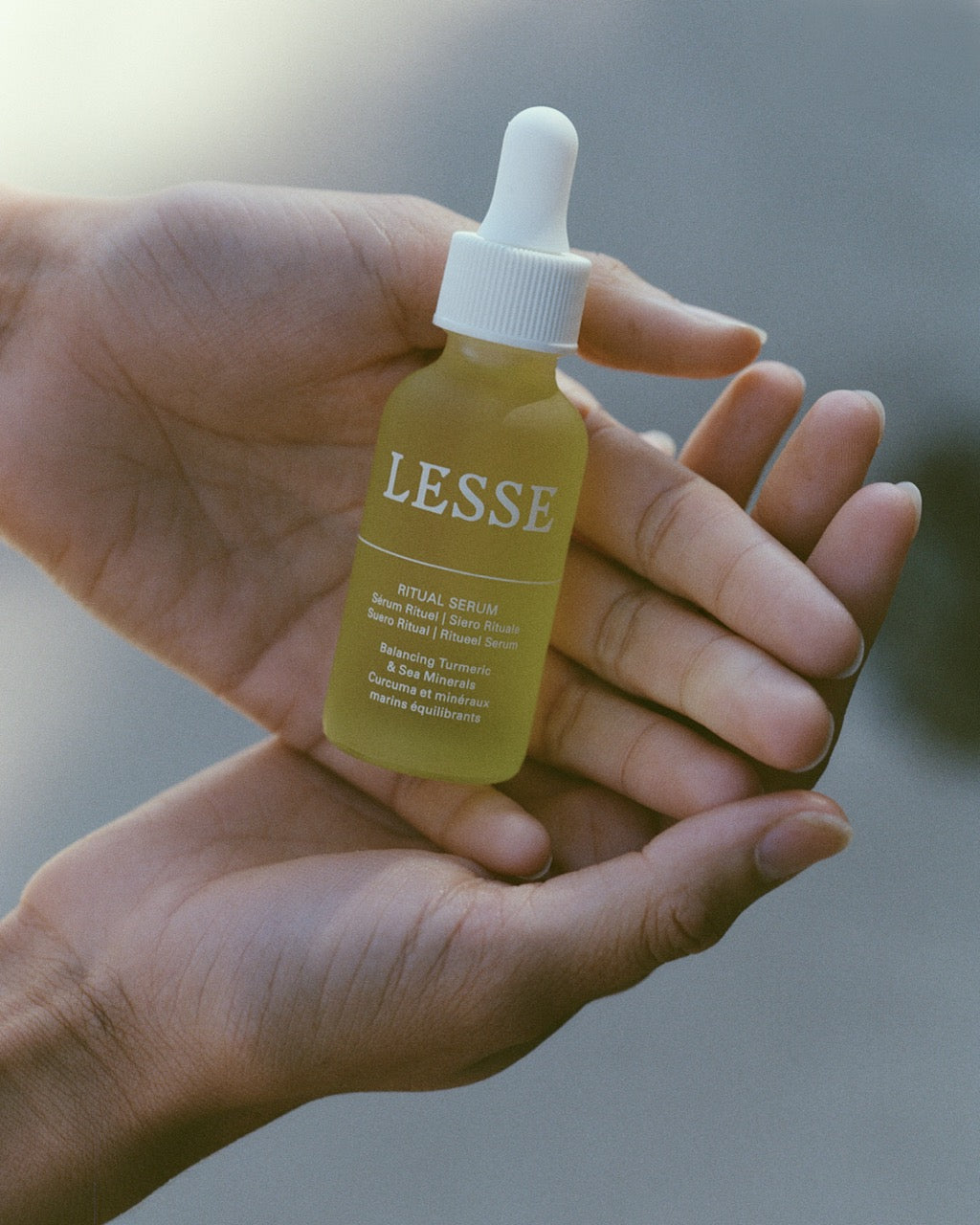 Hand holding a yellow LESSE serum bottle against a blurred background
