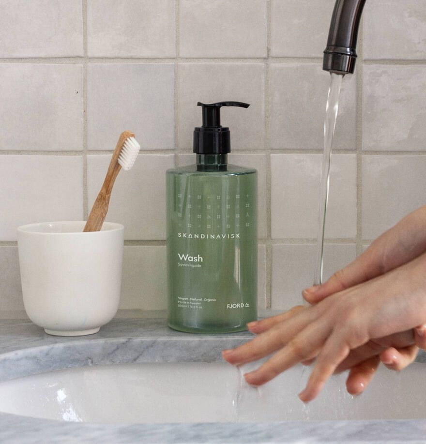 Person washing hands with a green bottle labeled 'Wash' in a bathroom setting.