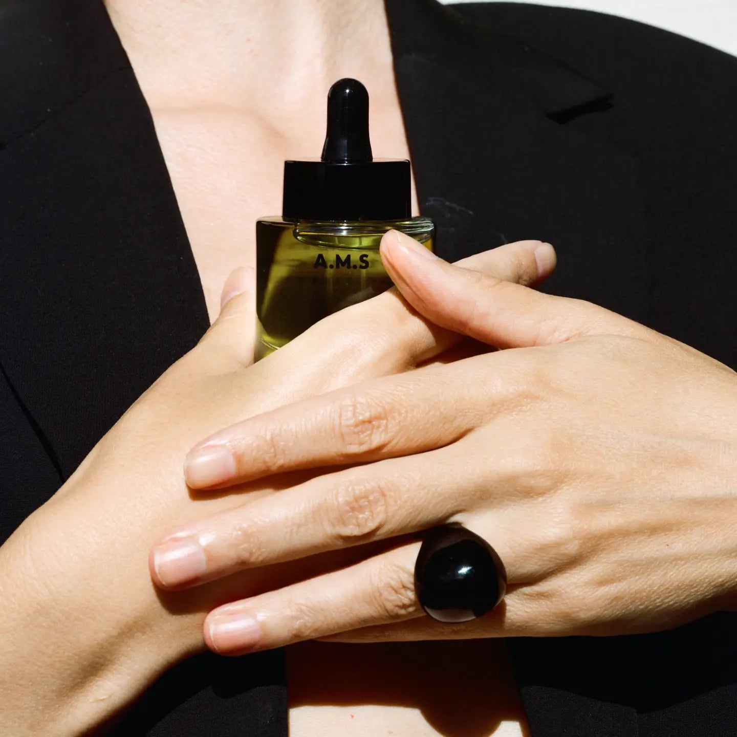 Person holding a bottle of A.M.S. skincare product with a black dropper.