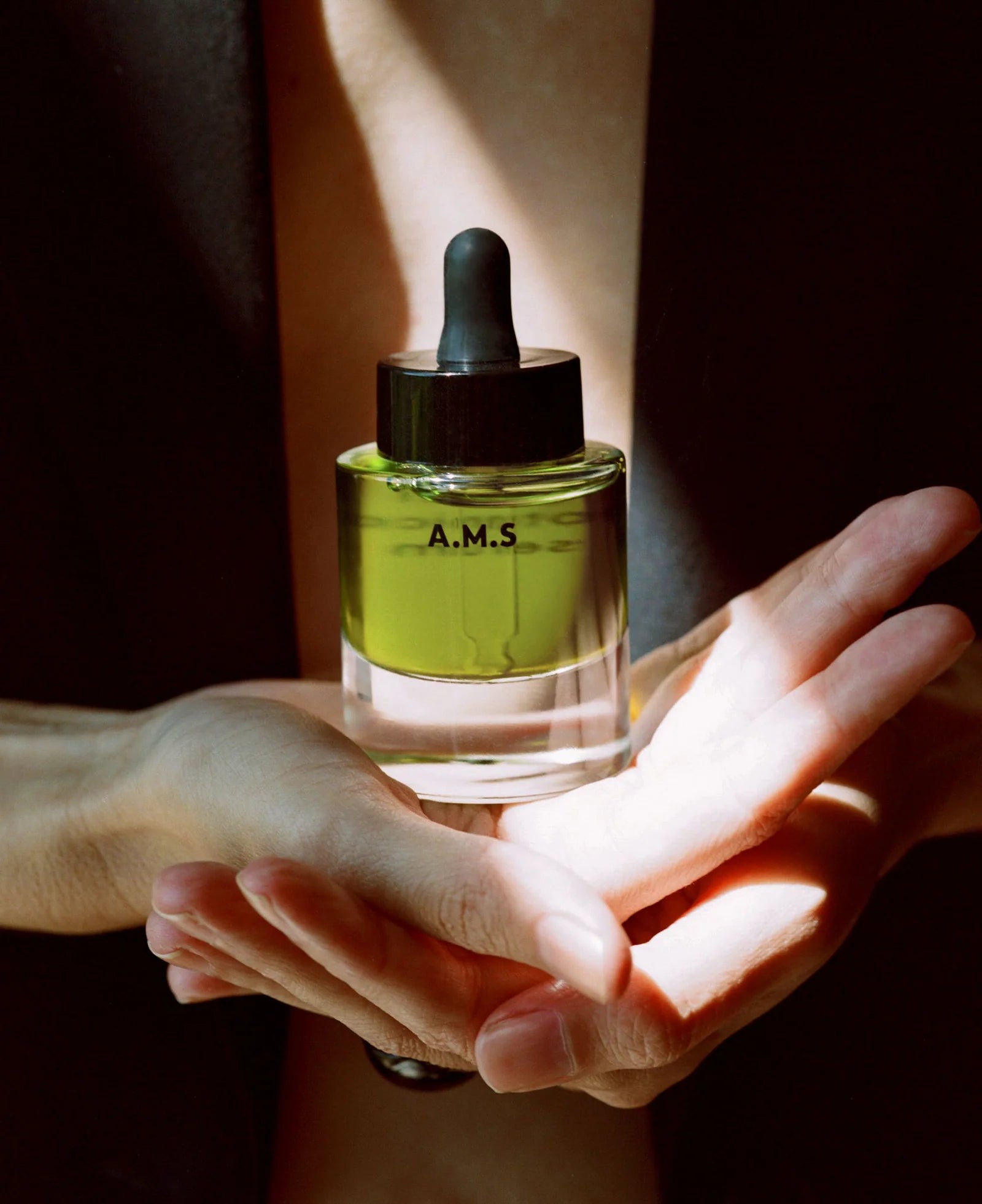 Bottle of A.M.S. skincare product held over a hand