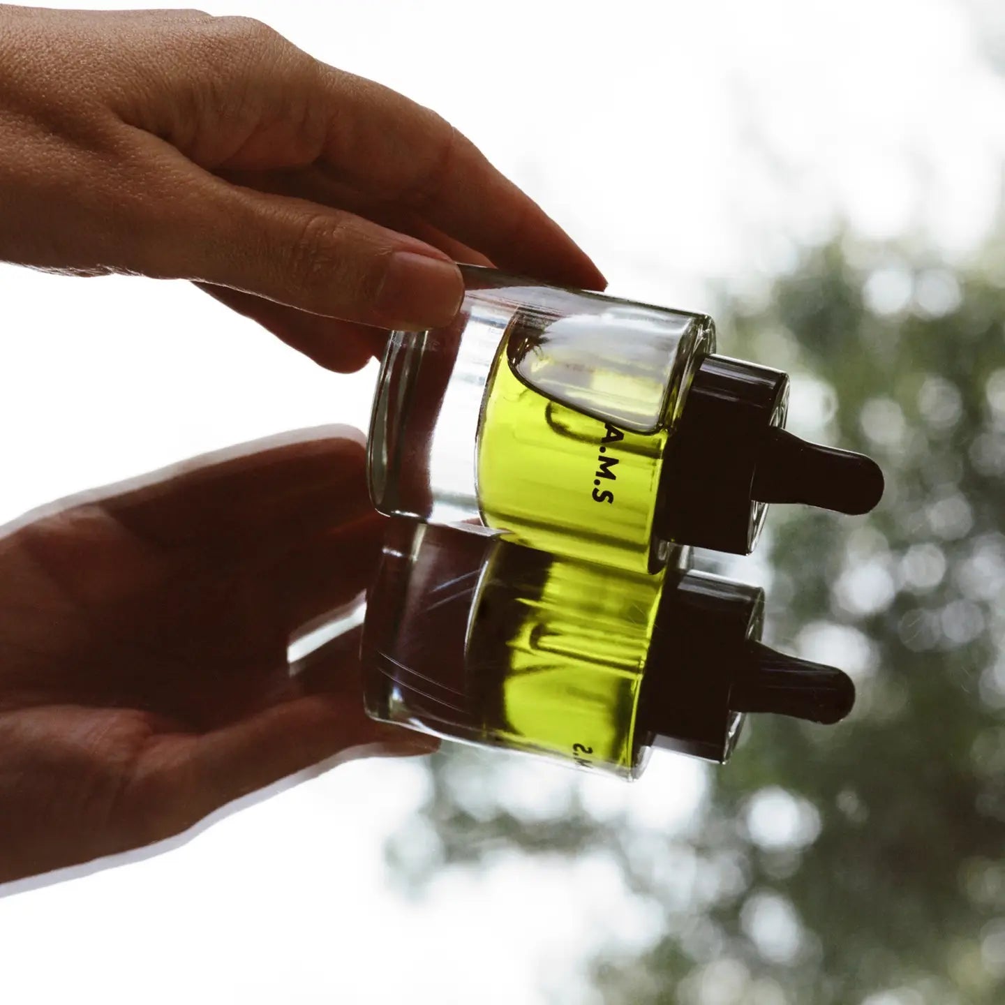 Hand holding a clear container with a A.M.S. Serum against a blurred natural background