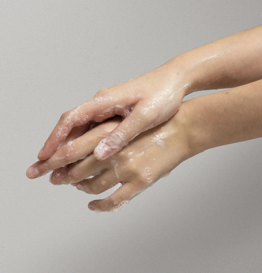 Hands with soap suds on a plain background