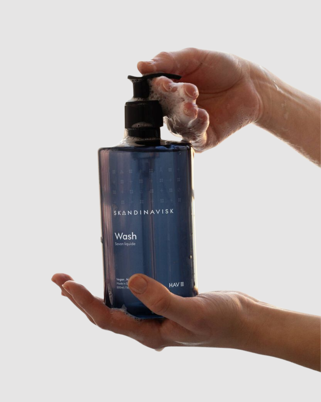 Person holding a blue bottle labeled 'Wash' by Skandinavisk against a light background