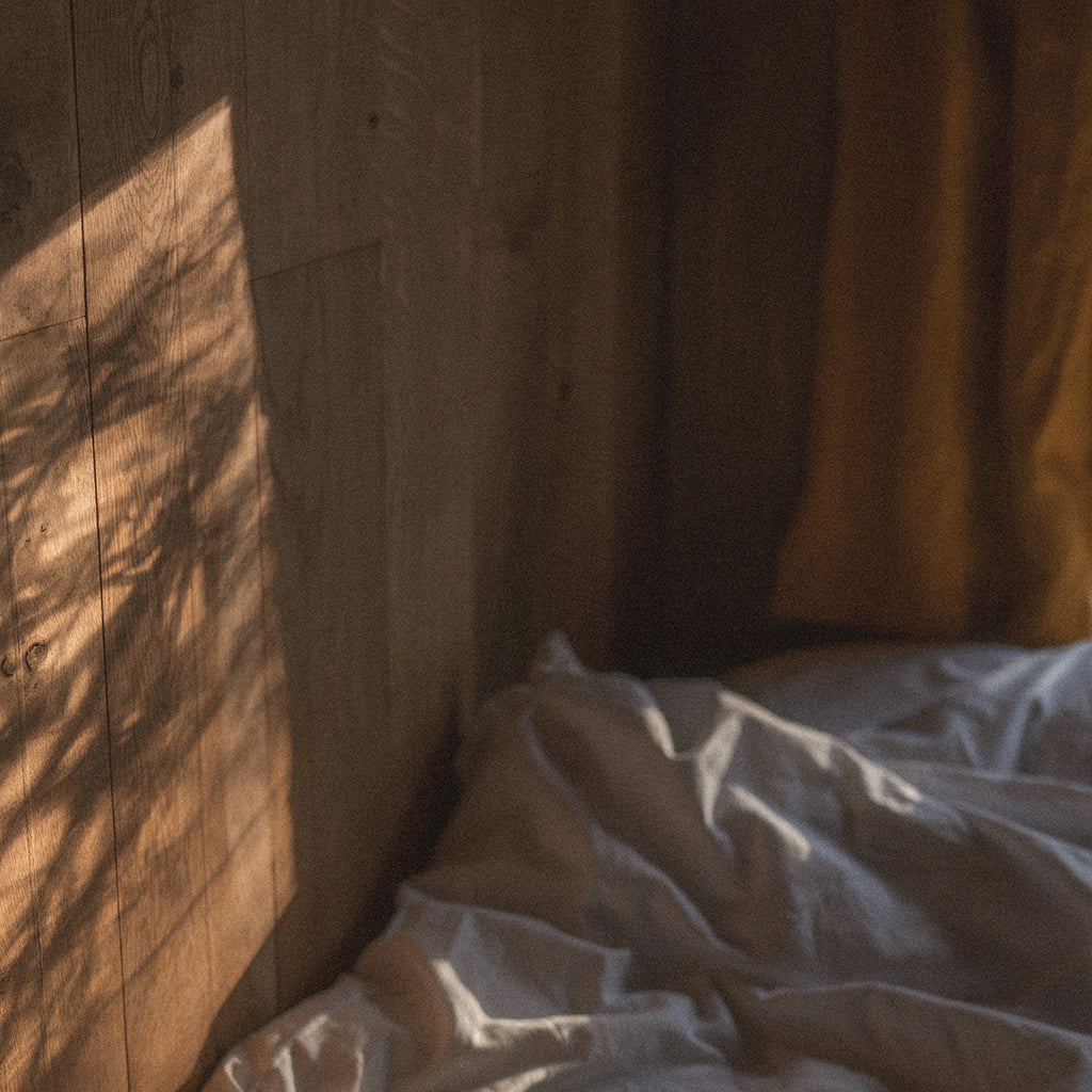 Sunlight filtering through a curtain onto a wooden wall with white bedding.