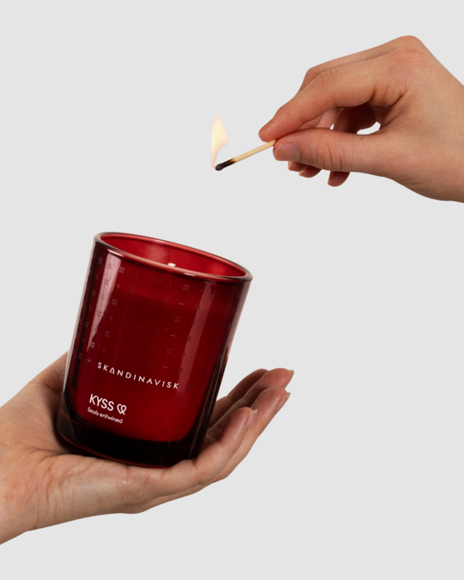 Person lighting a red candle with 'Skandinavisk' branding on a light gray background